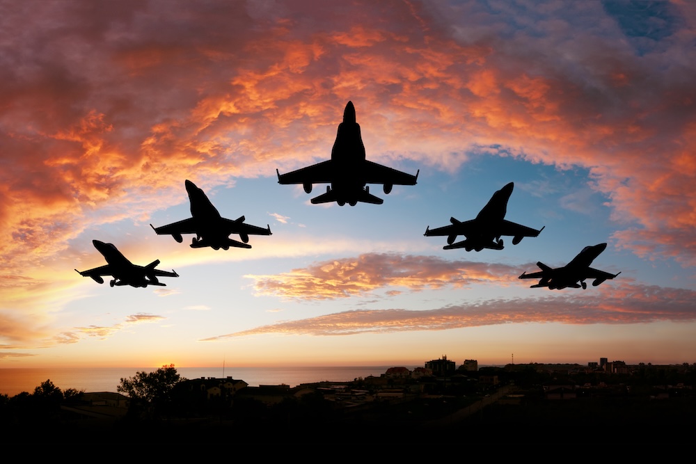 military planes flying in a V formation against a sunset sky